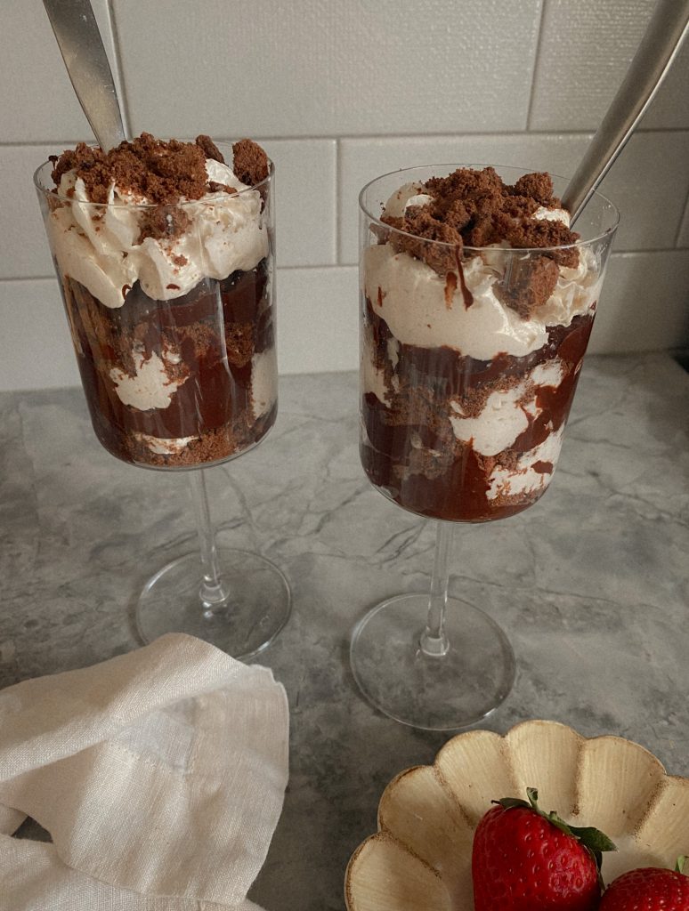 Vegan Chocolate Pudding in a Wine glass on a granite counter with coconut cool whip and crushed chocolate cookie crumble. For a Vegan and Paleo Chocolate Pudding Recipe 