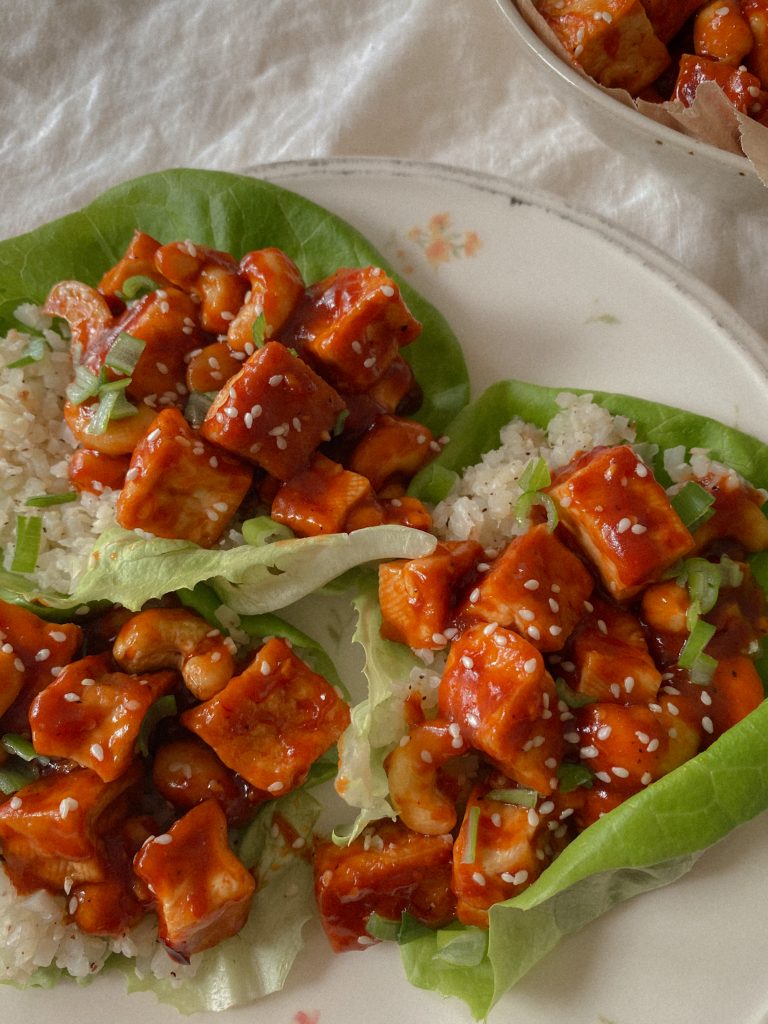 Vegan and Gluten Free Orange Cashew Chicken with sesame seeds served in lettuce wraps with white rice on a plate 