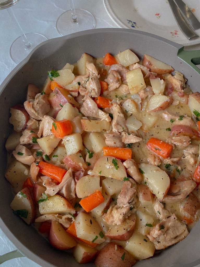 Chicken & Potatoes & Carrots in a creamy white wine sauce in a skillet with chopped carrots and herbs. 