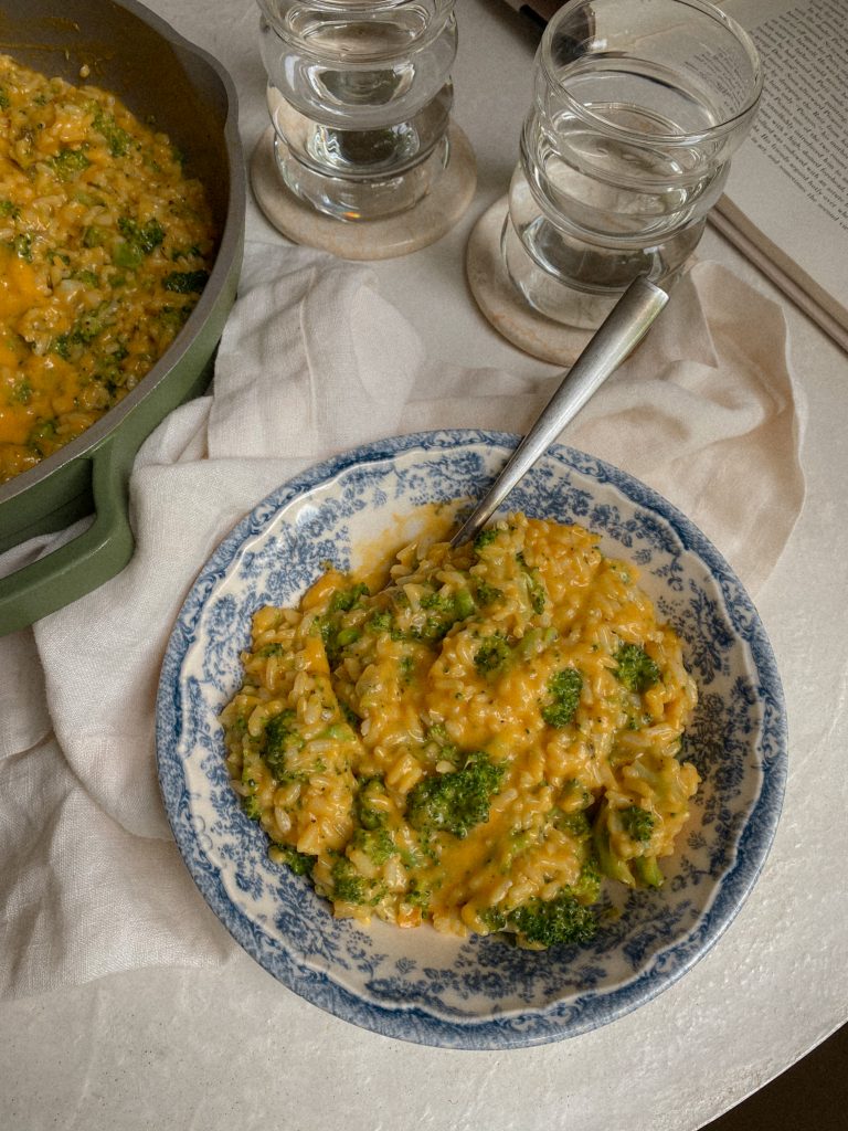 Gluten Free and Nut FreeCheesy Vegan Rice with Broccoli in a blue and white glass dish with spoon and bowl of the vegan cheesy broccoli rice recipe. 